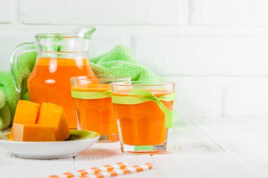 Güzel gözlük ve sürahi beyaz ahşap zemin üzerinde olgun sebze parçaları ile kabak taze meyve suyu. Tatlı portakal suyu. Sağlıklı beslenme, diyet Tema. Fotoğraf kadar kapatın. Yatay başlık