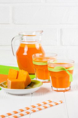 Güzel gözlük ve sürahi beyaz ahşap zemin üzerinde olgun sebze parçaları ile kabak taze meyve suyu. Tatlı portakal suyu. Sağlıklı beslenme, diyet Tema. Fotoğraf kadar kapatın. Dikey başlık