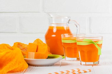 Güzel gözlük ve sürahi beyaz ahşap zemin üzerinde olgun sebze parçaları ile kabak taze meyve suyu. Tatlı portakal suyu. Sağlıklı beslenme, diyet Tema. Fotoğraf kadar kapatın. Yatay başlık