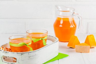 Güzel gözlük ve sürahi beyaz ahşap zemin üzerinde olgun sebze parçaları ile kabak taze meyve suyu. Tatlı portakal suyu. Sağlıklı beslenme, diyet Tema. Fotoğraf kadar kapatın. Yatay başlık