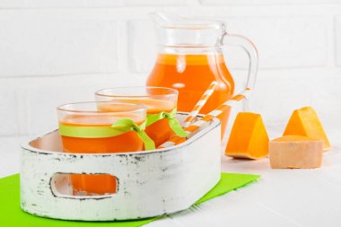 Güzel gözlük ve sürahi beyaz ahşap zemin üzerinde olgun sebze parçaları ile kabak taze meyve suyu. Tatlı portakal suyu. Sağlıklı beslenme, diyet Tema. Fotoğraf kadar kapatın. Yatay başlık