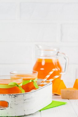 Güzel gözlük ve sürahi beyaz ahşap zemin üzerinde olgun sebze parçaları ile kabak taze meyve suyu. Tatlı portakal suyu. Sağlıklı beslenme, diyet Tema. Fotoğraf kadar kapatın. Dikey başlık