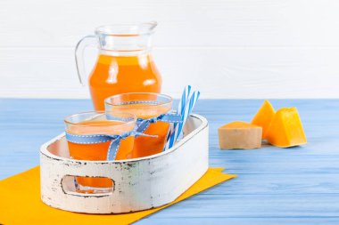 Güzel gözlük ve sürahi beyaz ahşap zemin üzerinde olgun sebze parçaları ile kabak taze meyve suyu. Tatlı portakal suyu. Sağlıklı beslenme, diyet Tema. Fotoğraf kadar kapatın. Yatay başlık