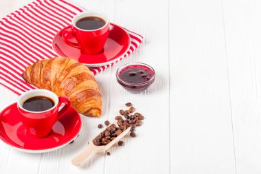 Taze pişmiş kruvasan peçete, Beyaz ahşap zemin üzerinde kırmızı Kupası kahve üzerinde. Fransız kahvaltı. Kahvaltı için taze hamur işleri. Lezzetli tatlı. Portre fotoğrafçılığı. Yatay başlık