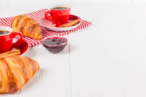 Freshly baked croissant on napkin, cup of coffee in red cup on white wooden background. French breakfast. Fresh pastries for breakfast. Delicious dessert. Closeup photography. Horizontal banner — Stock Photo, Image