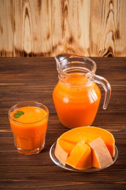 Güzel gözlük ve sürahi kahverengi ahşap zemin üzerinde olgun sebze parçaları ile kabak taze meyve suyu. Tatlı portakal suyu. Sağlıklı beslenme, diyet Tema. Fotoğraf kadar kapatın. Dikey başlık