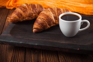 Kruvasan reçel, kahverengi ahşap zemin üzerinde beyaz fincan kahve fırından yeni çıkmış. Fransız kahvaltı. Kahvaltı için taze hamur işleri. Modern karanlık ruh tarzı. Lezzetli tatlı. Yatay başlık