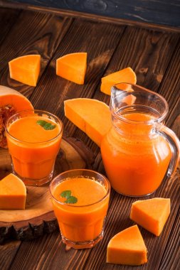 Güzel gözlük ve sürahi kahverengi ahşap zemin üzerinde olgun sebze parçaları ile kabak taze meyve suyu. Tatlı portakal suyu. Sağlıklı beslenme, diyet Tema. Fotoğraf kadar kapatın. Dikey başlık