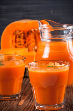 Güzel gözlük ve sürahi kahverengi ahşap zemin üzerinde olgun sebze parçaları ile kabak taze meyve suyu. Tatlı portakal suyu. Sağlıklı beslenme, diyet Tema. Fotoğraf kadar kapatın. Dikey başlık