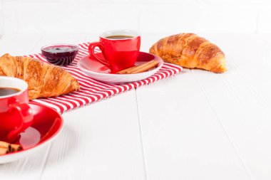 Taze pişmiş kruvasan peçete, Beyaz ahşap zemin üzerinde kırmızı Kupası kahve üzerinde. Fransız kahvaltı. Kahvaltı için taze hamur işleri. Lezzetli tatlı. Portre fotoğrafçılığı. Yatay başlık