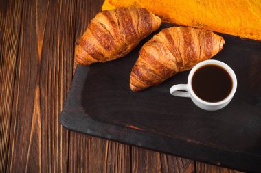 Kruvasan reçel, kahverengi ahşap zemin üzerinde beyaz fincan kahve fırından yeni çıkmış. Fransız kahvaltı. Kahvaltı için taze hamur işleri. Modern karanlık ruh tarzı. Lezzetli tatlı. Yatay başlık