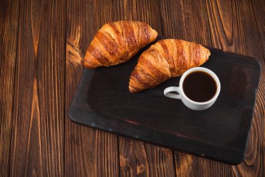 Kruvasan reçel, kahverengi ahşap zemin üzerinde beyaz fincan kahve fırından yeni çıkmış. Fransız kahvaltı. Kahvaltı için taze hamur işleri. Modern karanlık ruh tarzı. Lezzetli tatlı. Yatay başlık
