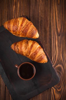 Kruvasan reçel, kahverengi ahşap zemin üzerinde beyaz fincan kahve fırından yeni çıkmış. Fransız kahvaltı. Kahvaltı için taze hamur işleri. Modern karanlık ruh tarzı. Lezzetli tatlı. Dikey başlık