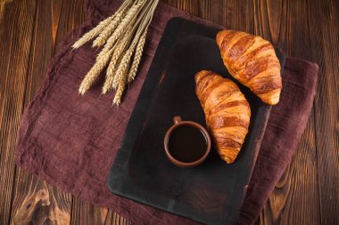 Kruvasan reçel, kahverengi ahşap zemin üzerinde beyaz fincan kahve fırından yeni çıkmış. Fransız kahvaltı. Kahvaltı için taze hamur işleri. Modern karanlık ruh tarzı. Lezzetli tatlı. Yatay başlık