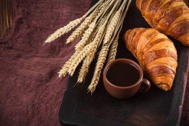 Kruvasan reçel, kahverengi ahşap zemin üzerinde beyaz fincan kahve fırından yeni çıkmış. Fransız kahvaltı. Kahvaltı için taze hamur işleri. Modern karanlık ruh tarzı. Lezzetli tatlı. Yatay başlık