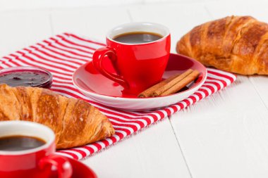 Taze pişmiş kruvasan peçete, Beyaz ahşap zemin üzerinde kırmızı Kupası kahve üzerinde. Fransız kahvaltı. Kahvaltı için taze hamur işleri. Lezzetli tatlı. Portre fotoğrafçılığı. Yatay başlık