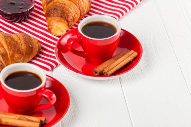 Taze pişmiş kruvasan peçete, Beyaz ahşap zemin üzerinde kırmızı Kupası kahve üzerinde. Fransız kahvaltı. Kahvaltı için taze hamur işleri. Lezzetli tatlı. Portre fotoğrafçılığı. Yatay başlık