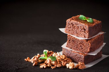 Çikolatalı kek kare parçalar halinde ceviz, beyaz plaka üzerine nane yaprakları ve siyah arka plan üzerine kakao ile dekore edilmiştir. Lezzetli tatlı. Karanlık ruh. Fotoğraf kadar kapatın. Seçici odak