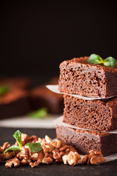 Выбирайте квадратные кусочки в стопку на белой тарелке с грецкими орехами, украшенные листьями мяты и кокосом на черном фоне. Вкусный десерт. Темное настроение. Закройте фотографию. Селективный фокус
