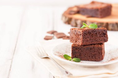 Çikolatalı kek kare parçalar halinde beyaz plaka üzerine nane yaprakları ve beyaz vintage ahşap zemin üzerine kakao tozu ile dekore edilmiştir. Amerikan geleneksel lezzetli tatlı. Fotoğraf kadar kapatın