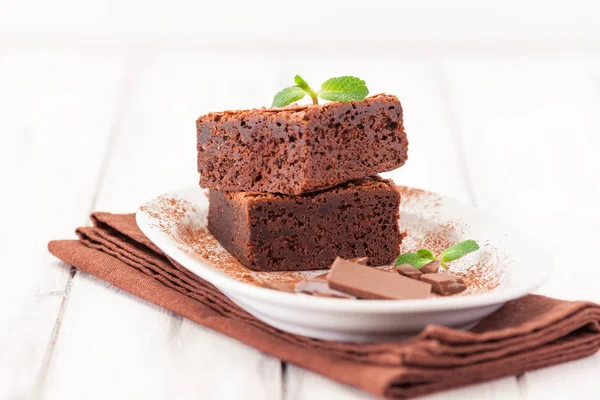 Chocolate brownie piezas cuadradas en pila en plato blanco decorado con hojas de menta y cacao en polvo sobre fondo de madera vintage blanco. Postre americano tradicional delicioso. Fotografía de cerca — Foto de Stock