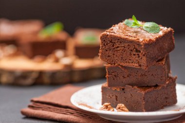 Çikolatalı kek kare parçalar halinde ceviz, beyaz plaka üzerine nane yaprakları ve siyah arka plan üzerine kakao ile dekore edilmiştir. Lezzetli tatlı. Karanlık ruh. Fotoğraf kadar kapatın. Seçici odak