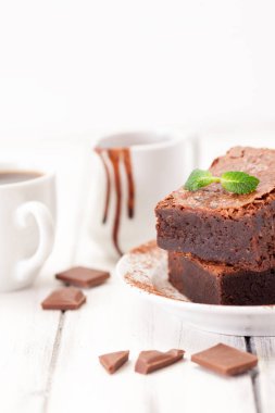 Çikolatalı kek kare parçalar halinde beyaz plaka üzerine nane yaprakları ve beyaz vintage ahşap zemin üzerine kakao tozu ile dekore edilmiştir. Amerikan geleneksel lezzetli tatlı. Fotoğraf kadar kapatın