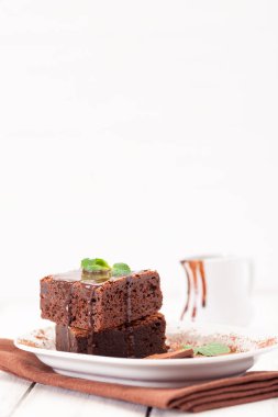 Çikolatalı kek kare parçalar halinde beyaz plaka üzerine nane yaprakları ve beyaz vintage ahşap zemin üzerine kakao tozu ile dekore edilmiştir. Amerikan geleneksel lezzetli tatlı. Fotoğraf kadar kapatın