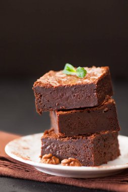 Çikolatalı kek kare parçalar halinde ceviz, beyaz plaka üzerine nane yaprakları ve siyah arka plan üzerine kakao ile dekore edilmiştir. Lezzetli tatlı. Karanlık ruh. Fotoğraf kadar kapatın. Seçici odak.