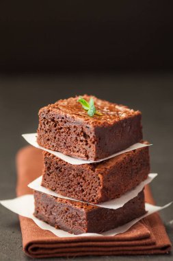 Çikolatalı kek kare parçalar halinde ceviz, beyaz plaka üzerine nane yaprakları ve siyah arka plan üzerine kakao ile dekore edilmiştir. Lezzetli tatlı. Karanlık ruh. Fotoğraf kadar kapatın. Seçici odak.