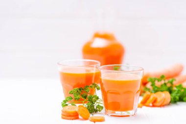 Havuç suyu güzel gözlük, kesim turuncu sebze ve Beyaz ahşap zemin üzerine yeşil maydanoz. Taze portakal suyu. Fotoğraf kadar kapatın. Seçici odak. Yatay başlık