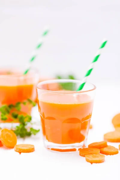 Succo di carota in bei bicchieri, verdure arancioni tagliate e prezzemolo verde su sfondo di legno bianco. Una bevanda all'arancia fresca. Chiudi la fotografia. Concentrazione selettiva. Bandiera verticale — Foto Stock