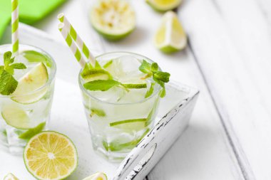 Caipirinha, mojito kireç, kahverengi şeker, buz ve nane ile kokteyl yaprakları yeşil narenciye Beyaz ahşap arka plan üzerinde kesme güzel gözlük. Yaz alkol içki. Fotoğraf kadar kapatın. Seçici odak