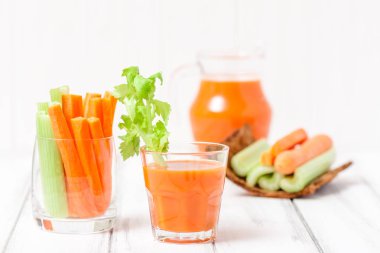 Havuç suyu güzel gözlük, kesilmiş havuç ve Beyaz ahşap arka plan ağaç kabuğu kase üzerinde yeşil kereviz. Taze sebze içki. Fotoğraf kadar kapatın. Seçici odak. Yatay başlık