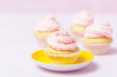 Cupcake pembe buttercream pastel pembe bir arka plan üzerinde parlak sarı plaka ile dekore edilmiştir. Tatlı güzel pasta. Yatay banner, tebrik kartı, tebrik. Fotoğraf kadar kapatın. Seçici odak