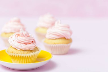 Cupcake pembe buttercream pastel pembe bir arka plan üzerinde parlak sarı plaka ile dekore edilmiştir. Tatlı güzel pasta. Yatay banner, tebrik kartı, tebrik. Fotoğraf kadar kapatın. Seçici odak
