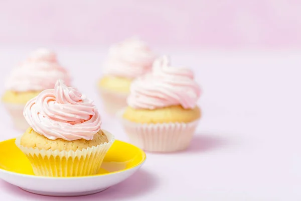 컵 케 익 핑크 buttercream 파스텔 분홍색 배경에 밝은 노란색 접시에 장식 되어 있습니다. 달콤한 아름 다운 케이크입니다. 수평 배너, 인사말 카드, 축 하입니다. 사진을 닫습니다. 선택적 초점 — 스톡 사진