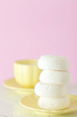 Zephyr'i dessrt pembe plaka, pastel pembe arka plan üzerine sütlü kahve fincan beyaz. Güzel tatlılar. Dikey afiş, tebrik kartı için doğum günü, düğün. Fotoğraf kadar kapatın. Seçici odak