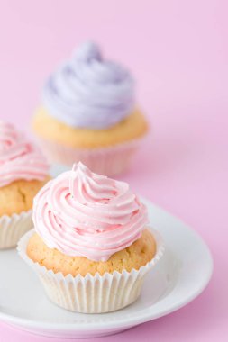Cupcake pastel pembe arka plan üzerine pembe ve mor buttercream ile dekore edilmiştir. Tatlı güzel pasta. Dikey afiş, tebrik kartı için doğum günü, düğün. Fotoğraf kadar kapatın. Seçici odak