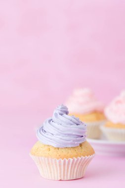 Cupcake pastel pembe arka plan üzerine pembe ve mor buttercream ile dekore edilmiştir. Tatlı güzel pasta. Dikey afiş, tebrik kartı için doğum günü, düğün. Fotoğraf kadar kapatın. Seçici odak