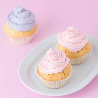 Cupcake pastel pembe arka plan üzerine pembe ve mor buttercream ile dekore edilmiştir. Tatlı güzel pasta. Kare afiş, tebrik kartı için doğum günü, düğün. Fotoğraf kadar kapatın. Seçici odak