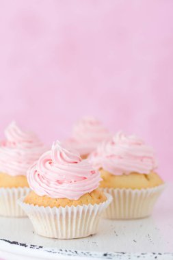 Pastel pembe bir arka plan üzerinde pembe buttercream süslenmiş cupcake.