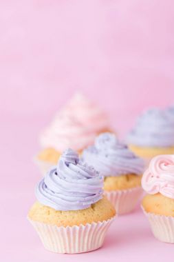 Pastel pembe bir arka plan üzerinde pembe ve mor buttercream duran Top kek süslenmiş