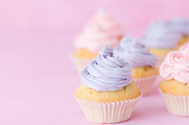 Pastel pembe bir arka plan üzerinde pembe ve mor buttercream duran ile cupcakes.