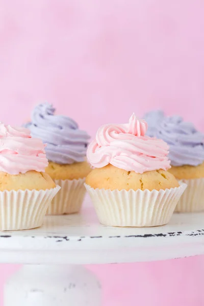 Cupcakes decorados con crema de mantequilla rosa y violeta en soporte shabby shic sobre fondo rosa pastel — Foto de Stock