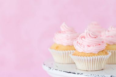 Eski püskü shic stand pastel güzel pembe arka plan üzerinde pembe buttercream süslenmiş cupcake.