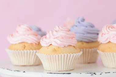 Pastel pembe bir arka plan üzerinde pembe ve mor buttercream duran ile cupcakes.