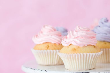 Pastel pembe bir arka plan üzerinde pembe ve mor buttercream duran ile cupcakes.