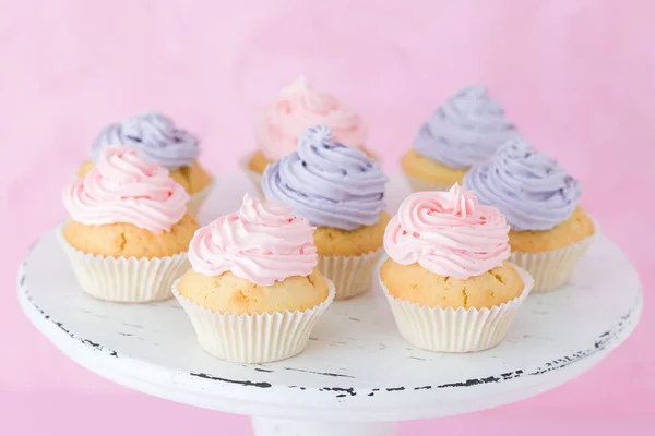 Cupcakes decorados con crema rosa y violeta sobre blanco shabby shic stand sobre fondo rosa pastel . — Foto de Stock