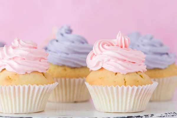 Gâteaux au beurre rose et violet debout sur fond rose pastel . — Photo